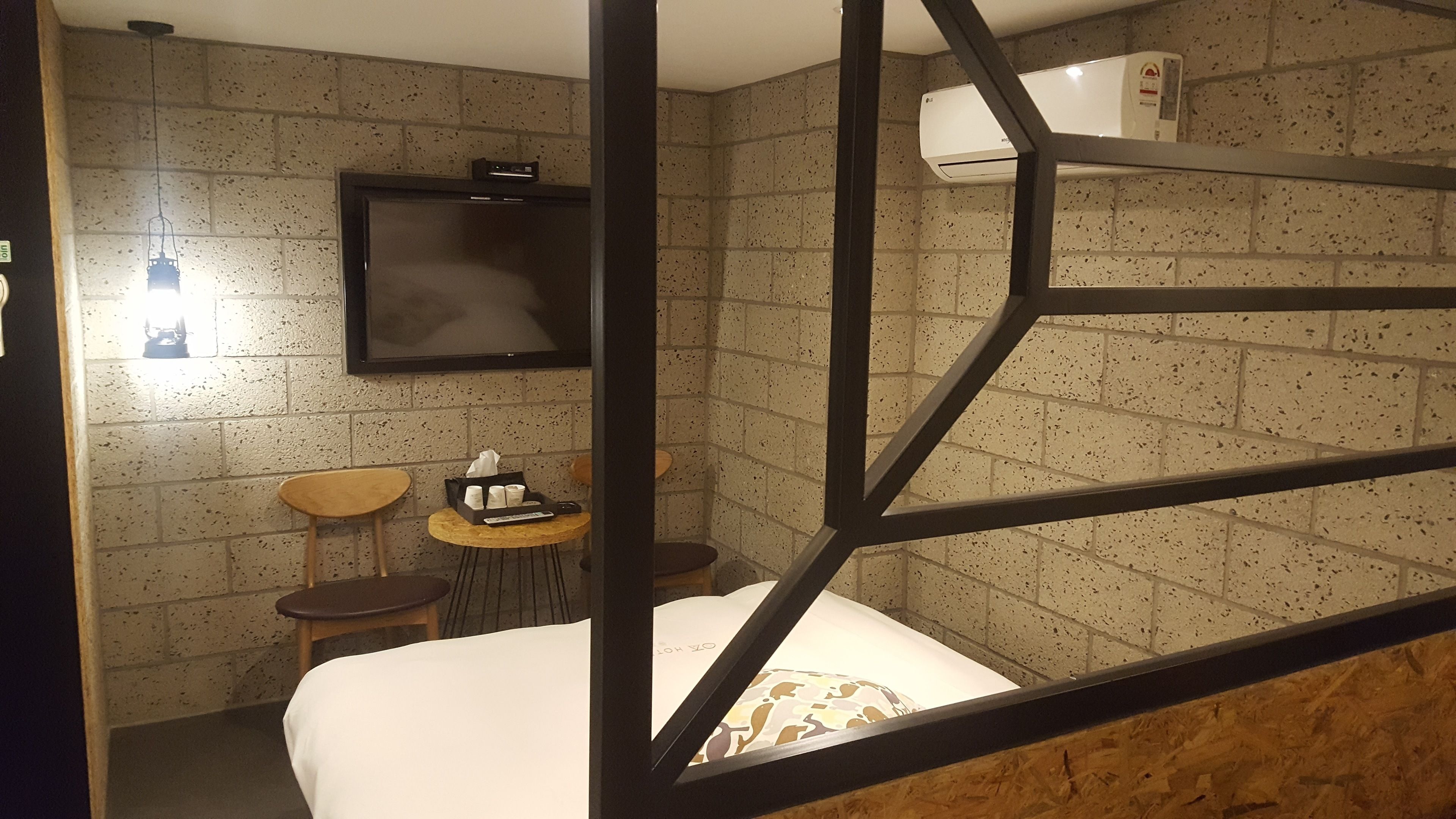A room with a bunk bed, a TV mounted on the wall, a small table with a remote control, and a wall-mounted air conditioner.