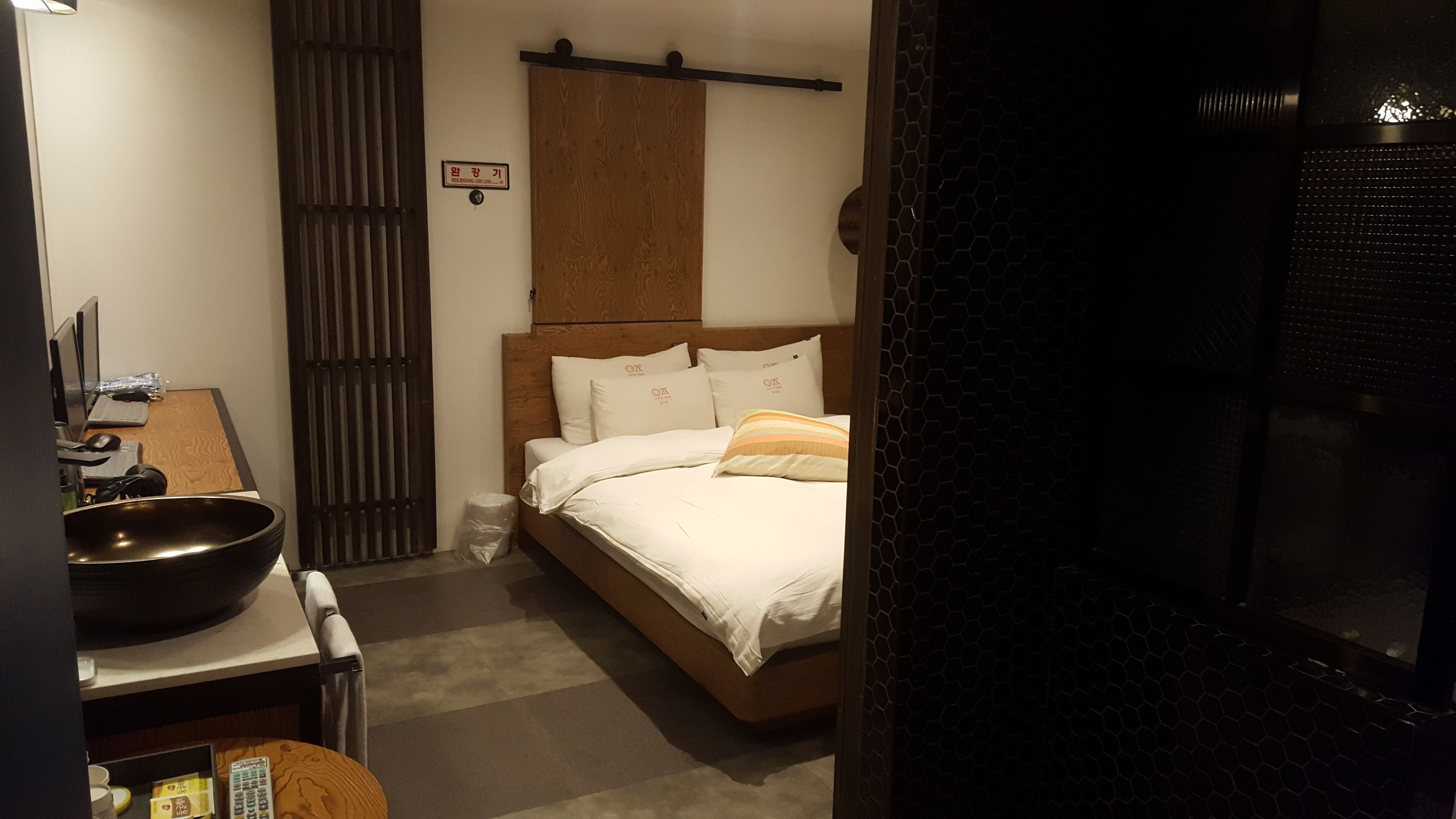 Una habitación de hotel con cama, escritorio con computadora y un amplio ventanal con vista a la ciudad.