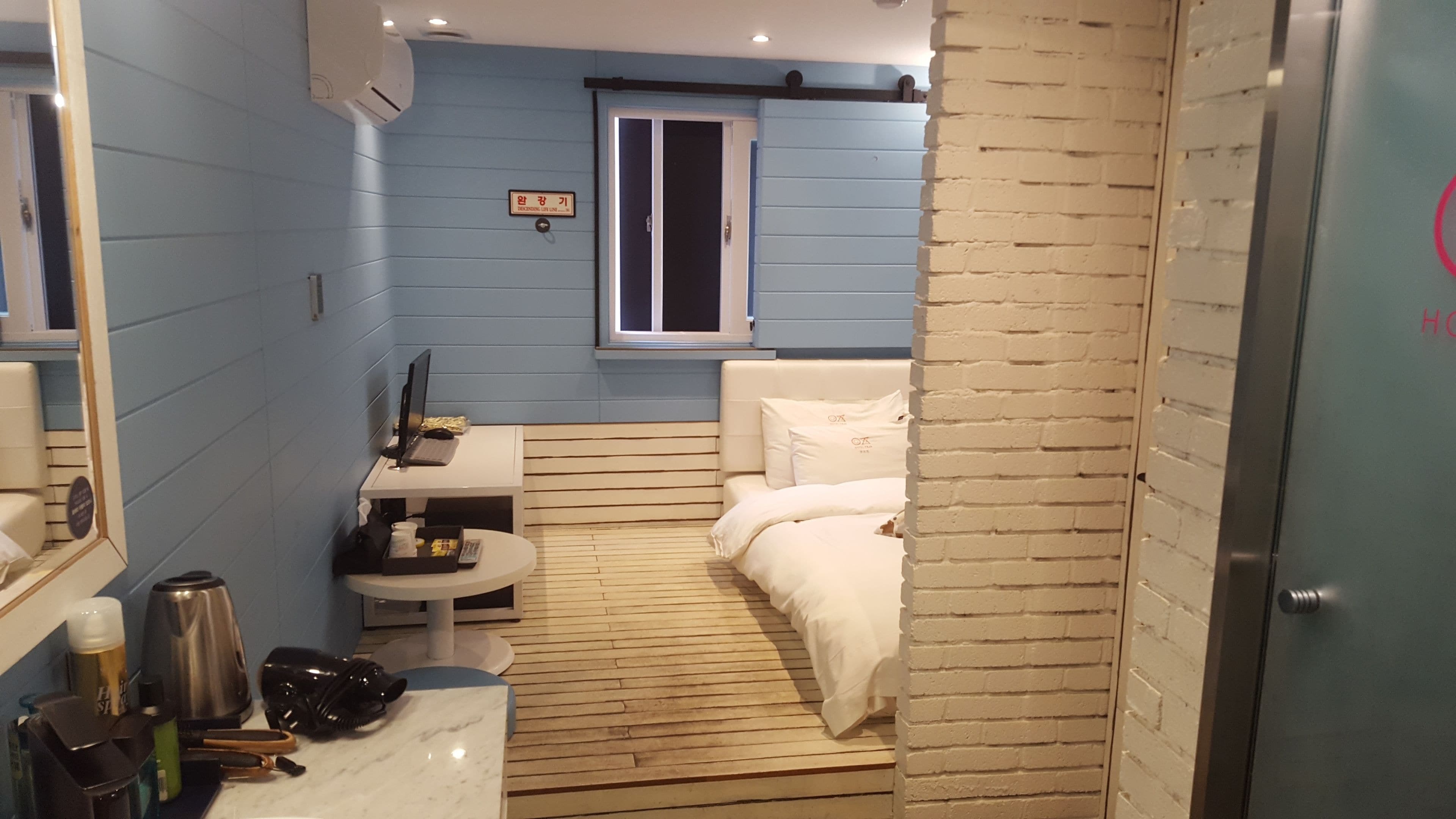 Habitación de hotel compacta con cama, un escritorio pequeño con computadora, ventana y zona de baño.