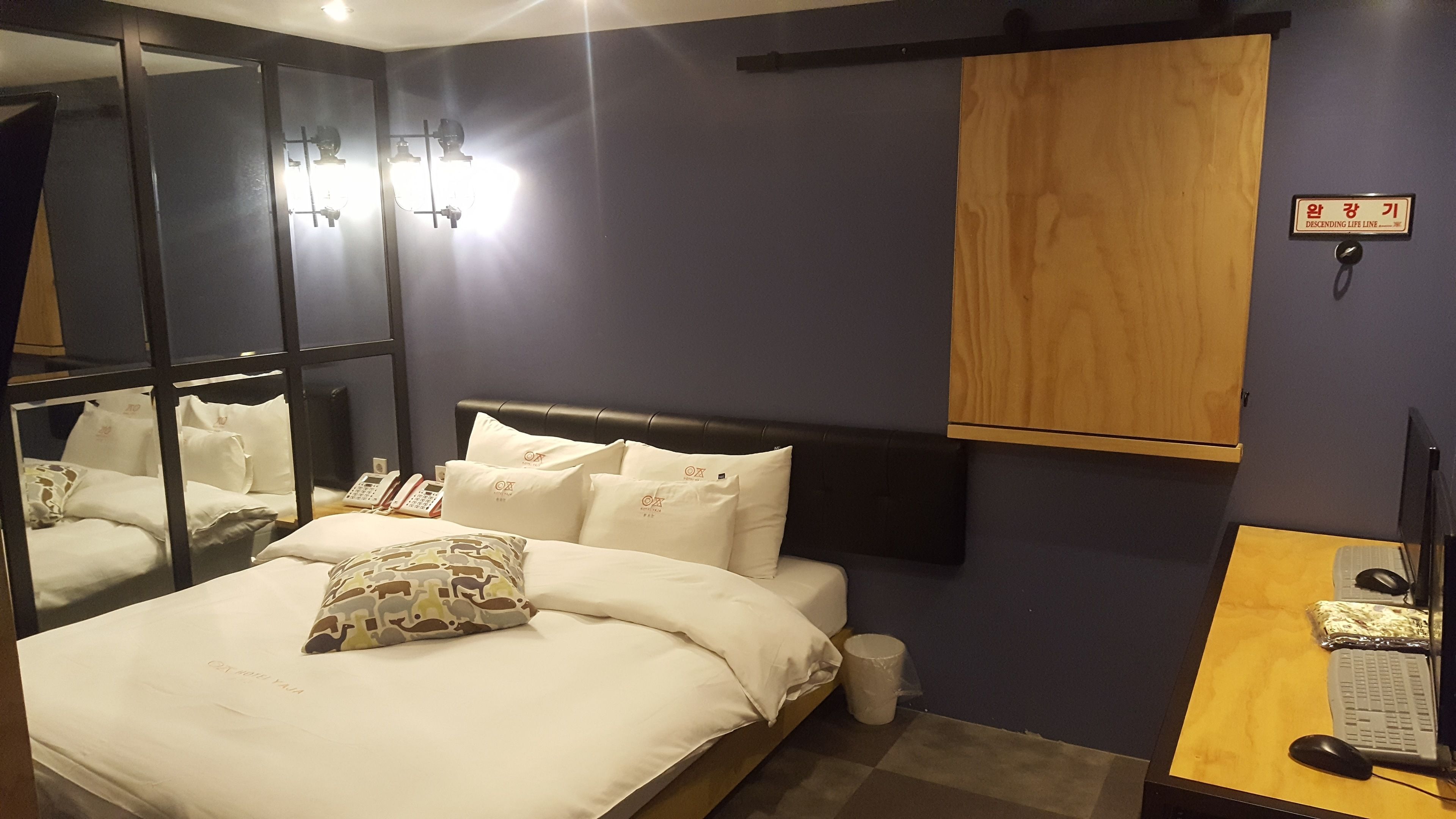 A hotel room with a bed, a desk with a computer, a mirror, and a wooden cabinet.