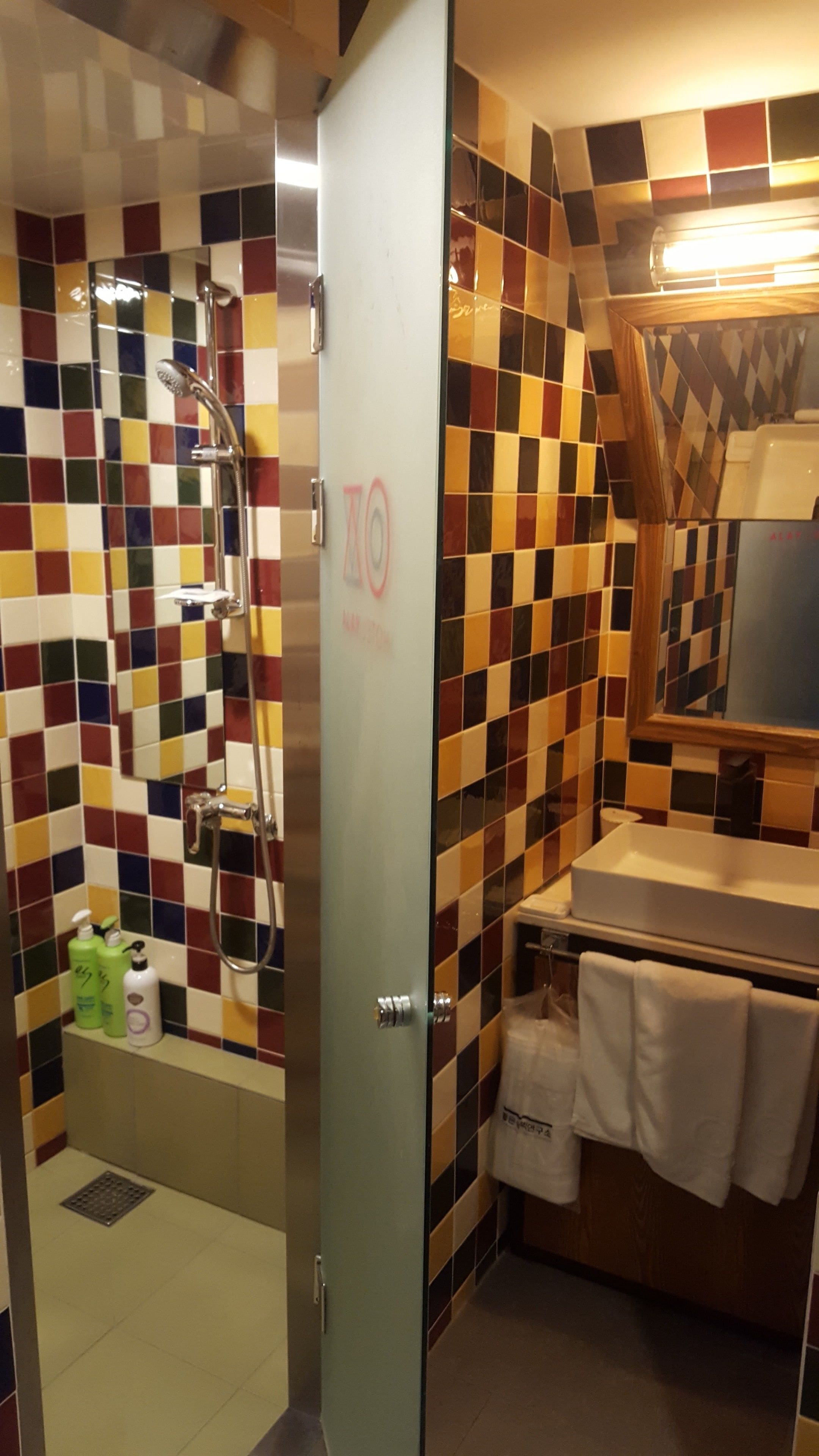 A bathroom with a shower, a sink, and a mirror. There are toiletries on the sink counter.