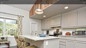 A kitchen with a central island, wooden chairs, a window with a view, and a microwave. - Bella Rosa Cottage - Stroll to Wimberley Square! Cypress Creek just steps away (Wimberley)