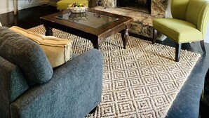 A living room with a stone fireplace, a television, and two green armchairs. - Bella Rosa Cottage - Stroll to Wimberley Square! Cypress Creek just steps away (Wimberley)