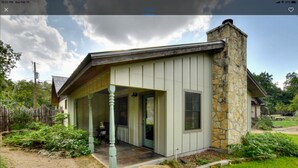 A single-story house with a stone chimney, a covered porch, and a front door. - Bella Rosa Cottage - Stroll to Wimberley Square! Cypress Creek just steps away (Wimberley)