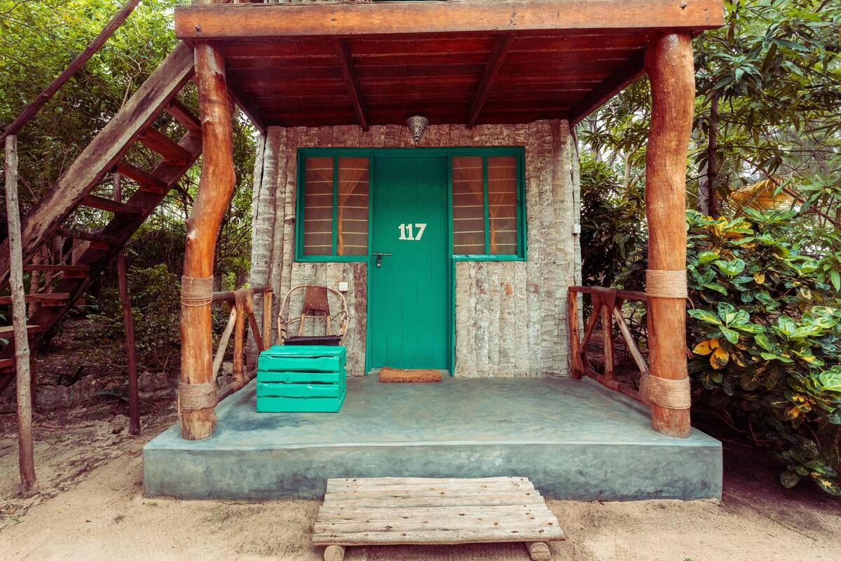 A rustic wooden structure with a green door, numbered 117, and a concrete platform.