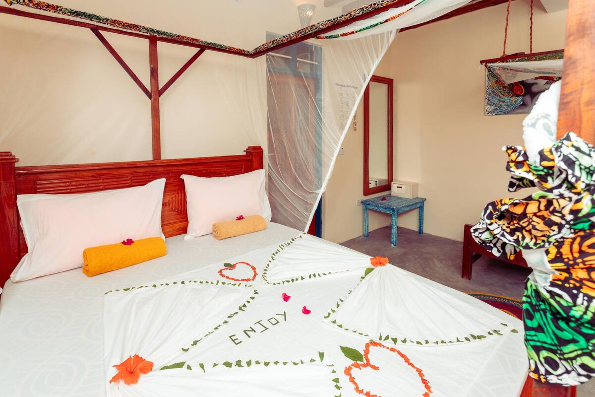 A bed with a canopy, a small table, and a chair in a room with a simple design.