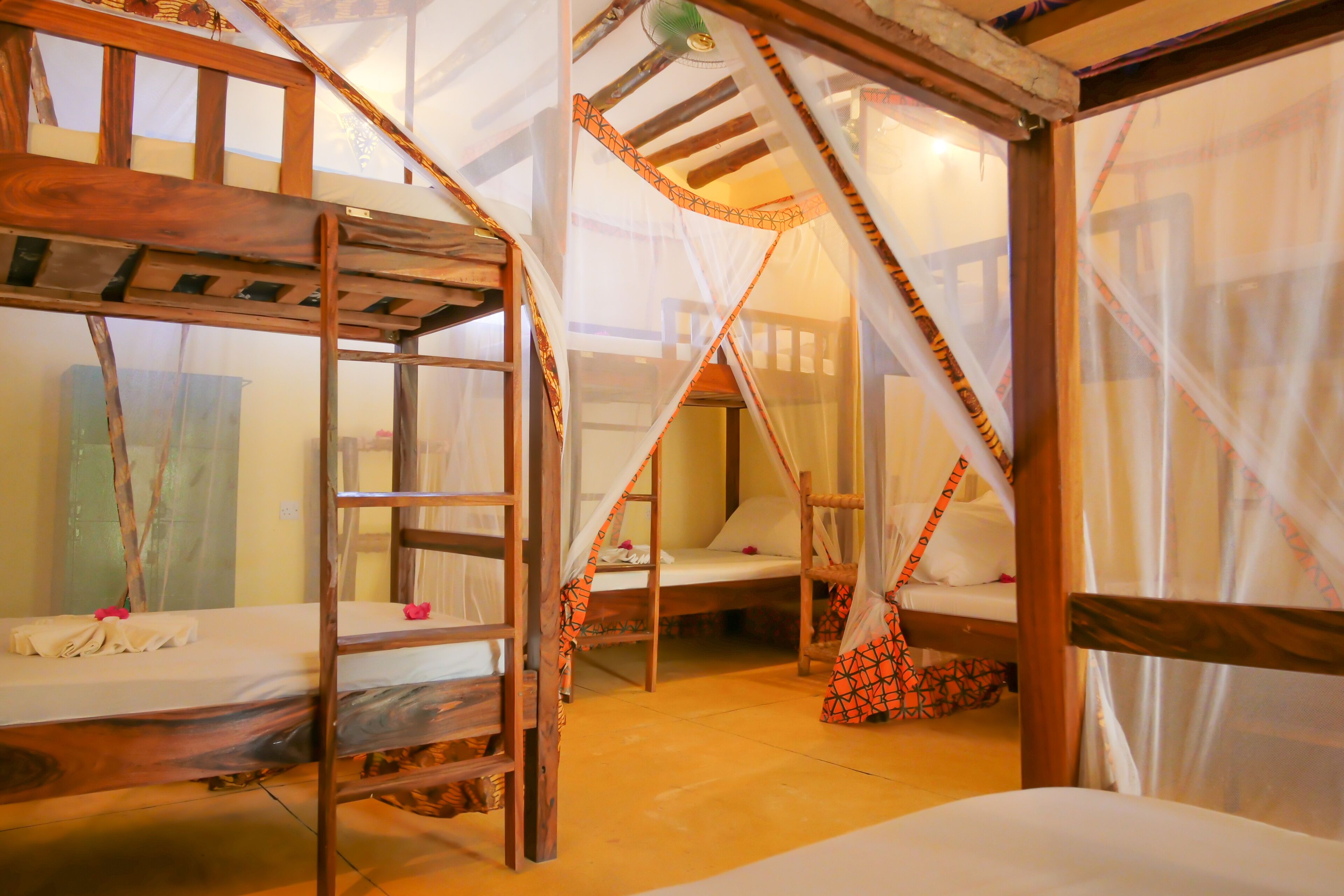 A room with bunk beds, wooden beams, and mosquito netting.