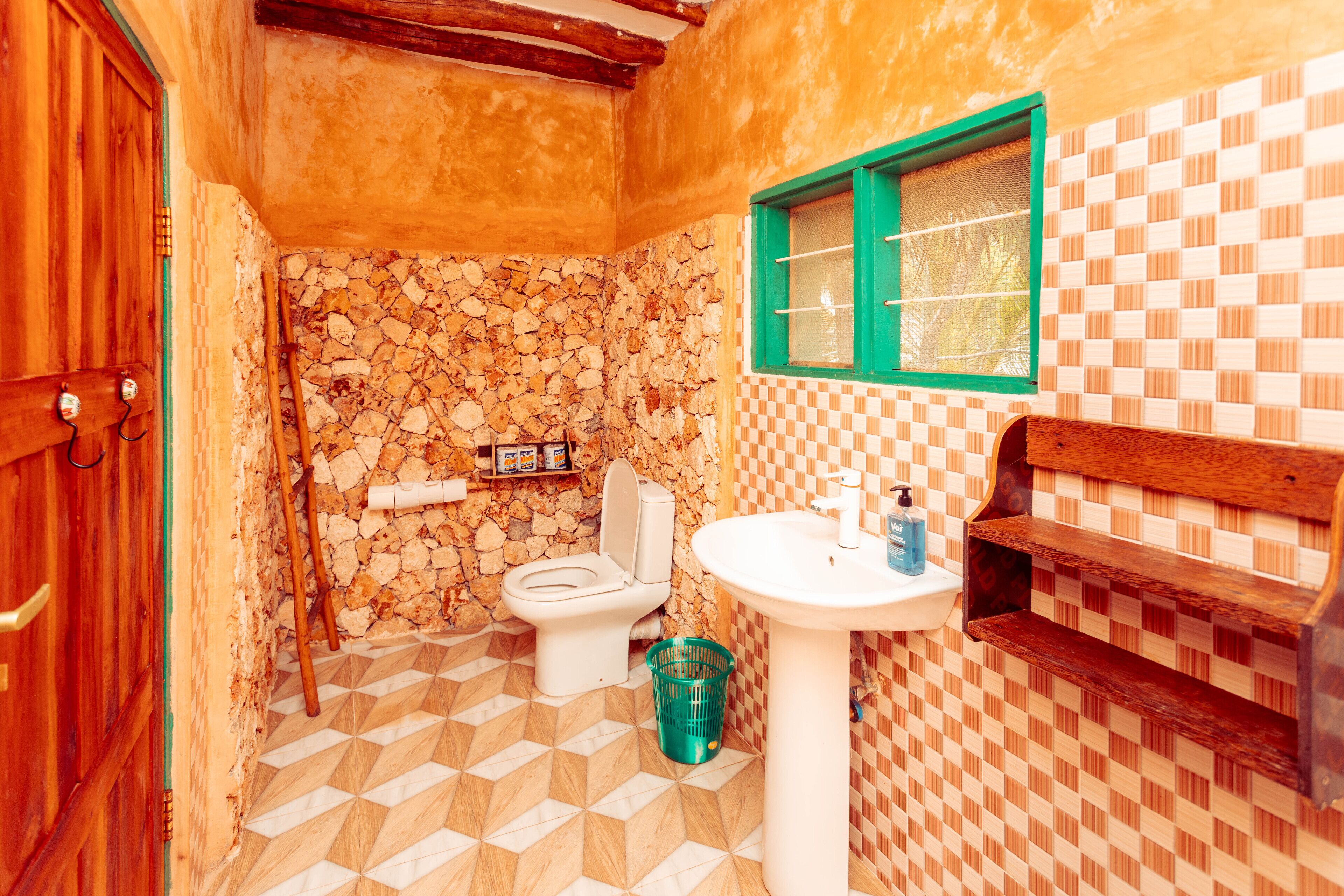 Un bagno con parete in pietra, un water, un lavabo e una mensola in legno.