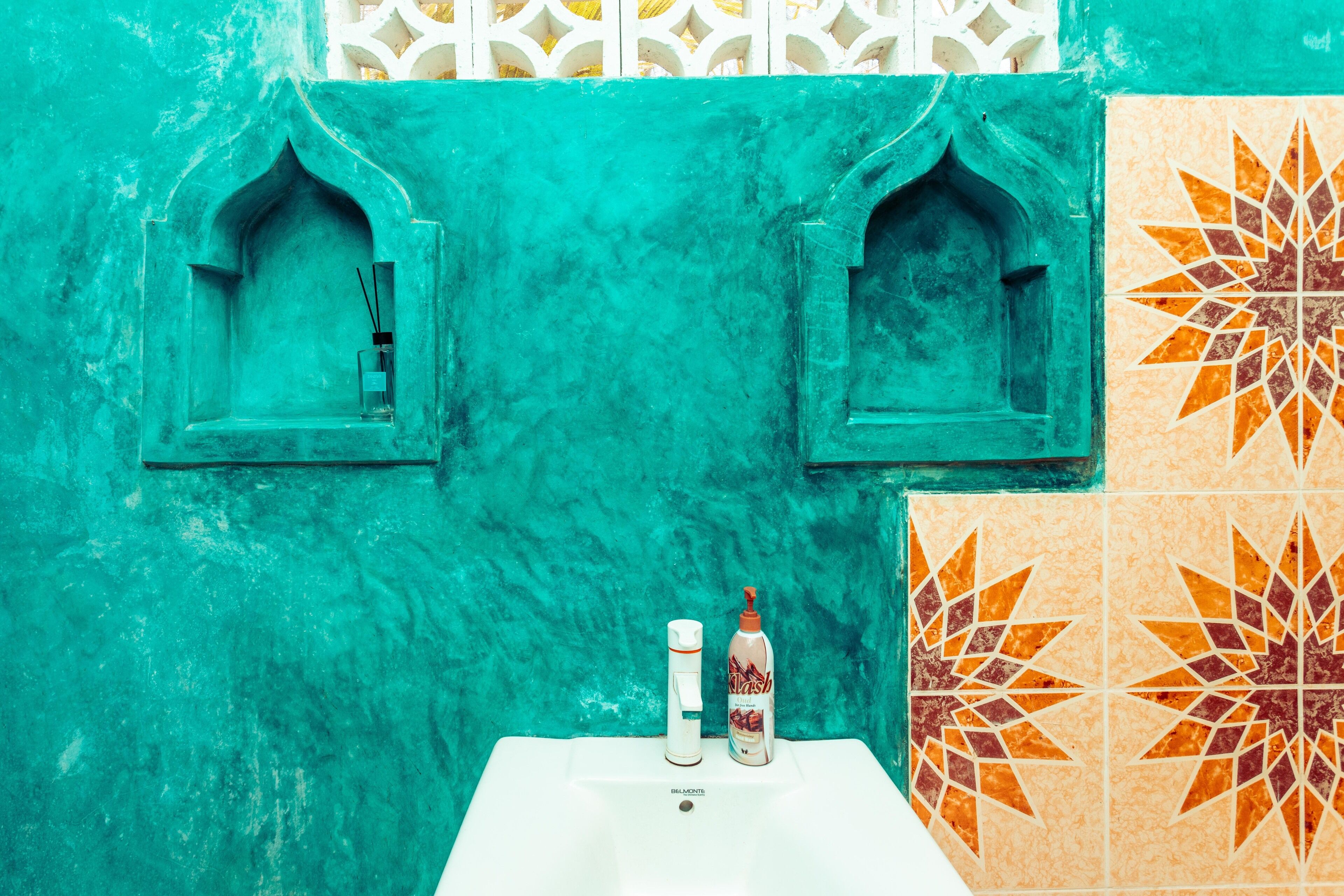 Une salle de bain avec un mur turquoise, un lavabo blanc et un flacon de savon liquide.