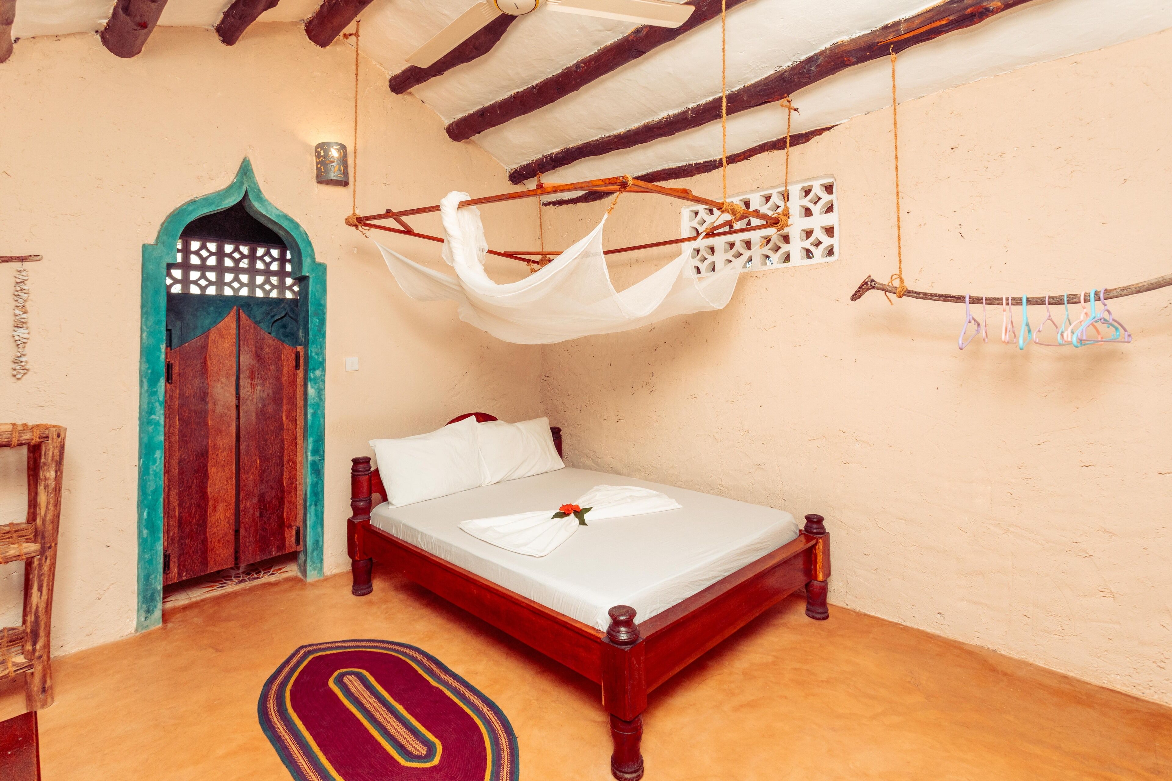 A traditional wooden bed with a white mattress, a colorful rug, and a unique hanging laundry rack.