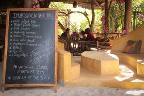 Un menú en pizarra para una barbacoa de jueves, con una lista de comidas y una nota sobre música en vivo.