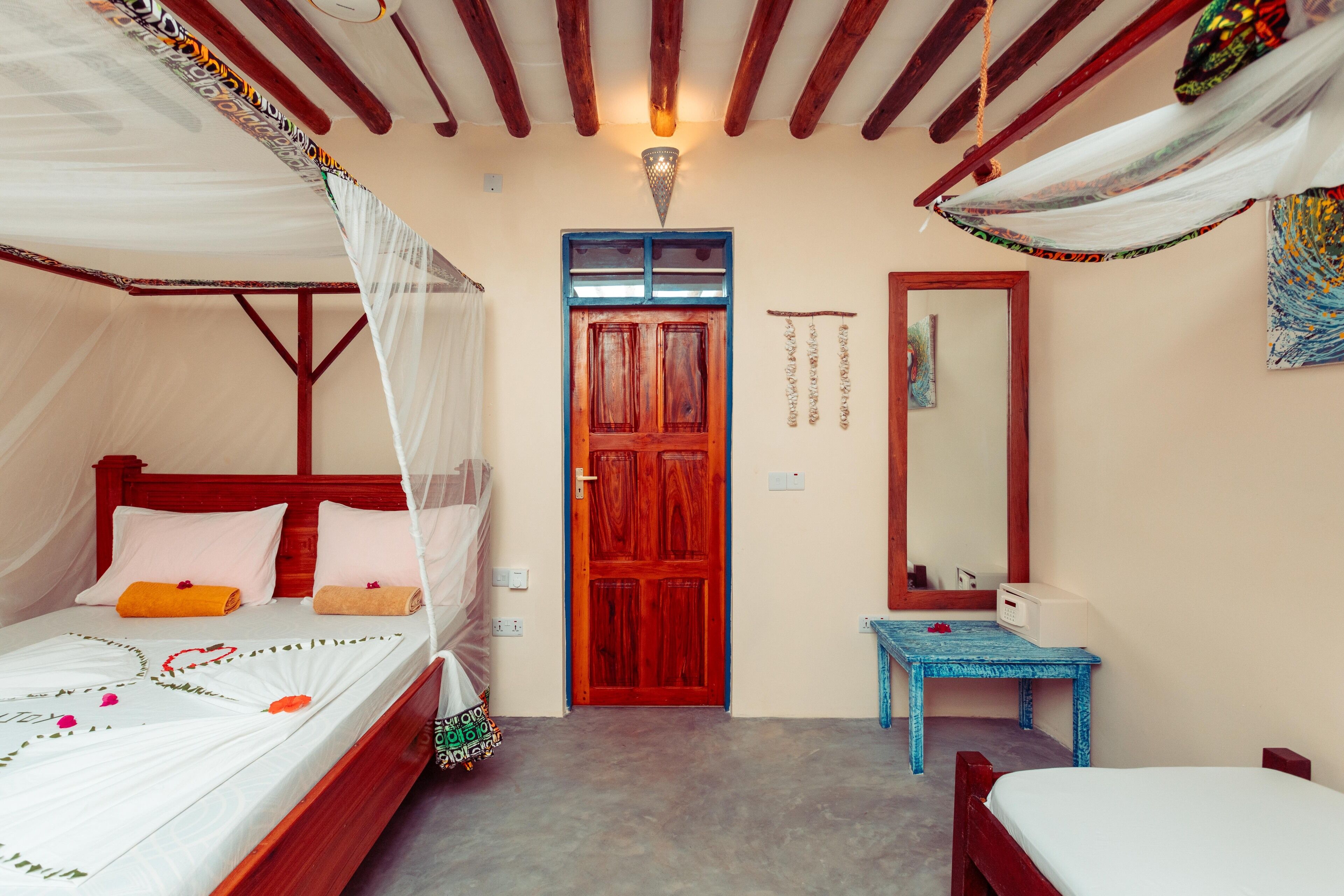 A room with a bed, a small table, a mirror, and a door.