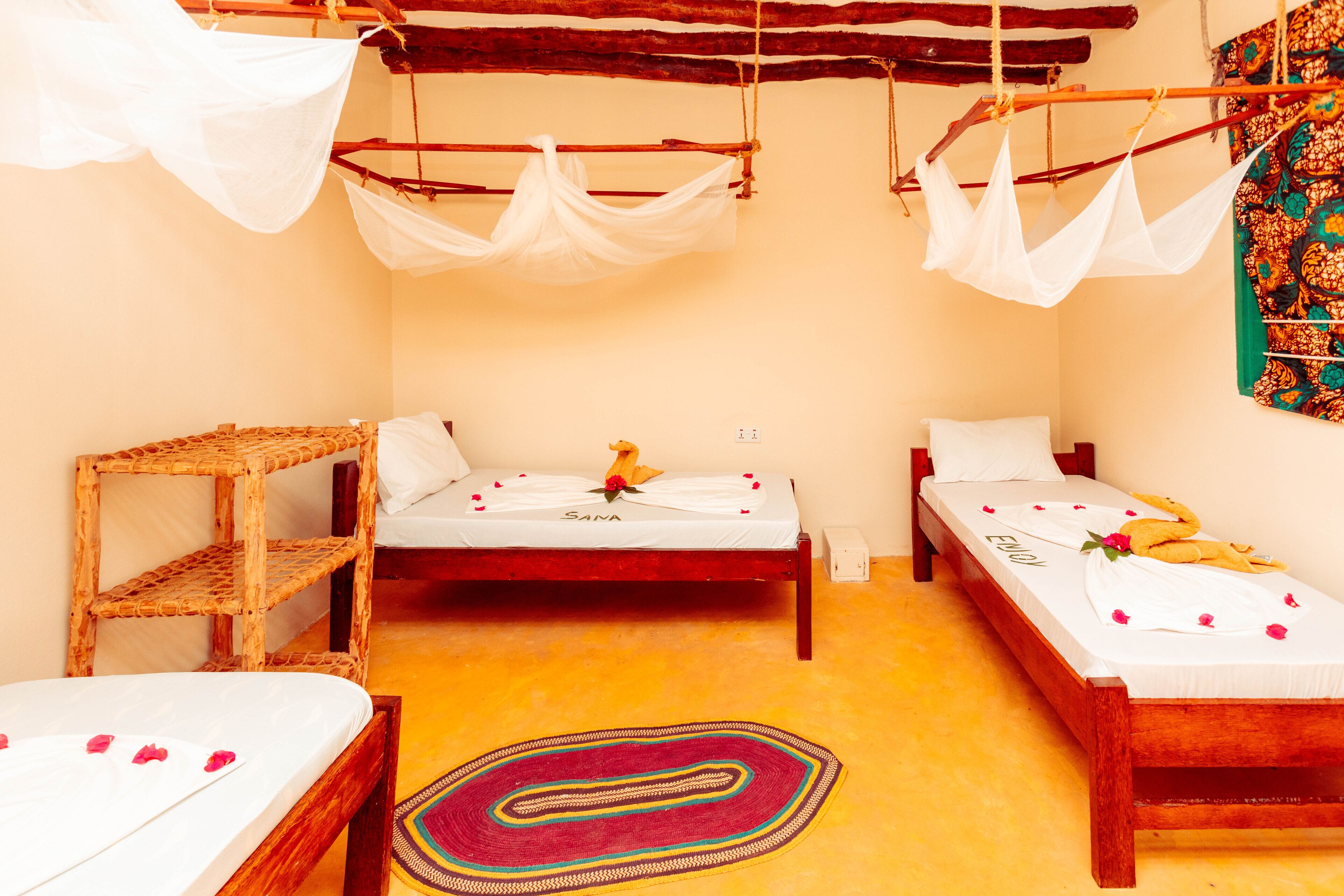 Ein Zimmer mit zwei Holzbetten, einer gewobenen Ablage, einem farbenfrohen Teppich und einem Baldachinbett.