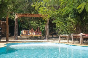 Relax by the serene pool surrounded by lush greenery and shaded by a wooden swing.