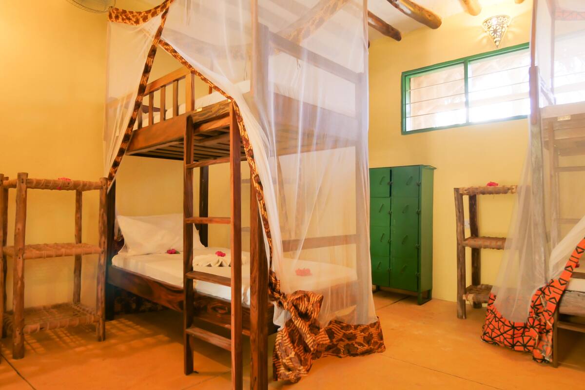 A room with two bunk beds, a green cabinet, and a mosquito net over the beds.