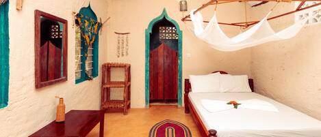 A traditional room with a bed, a wooden table, a bench, and a hanging mosquito net.