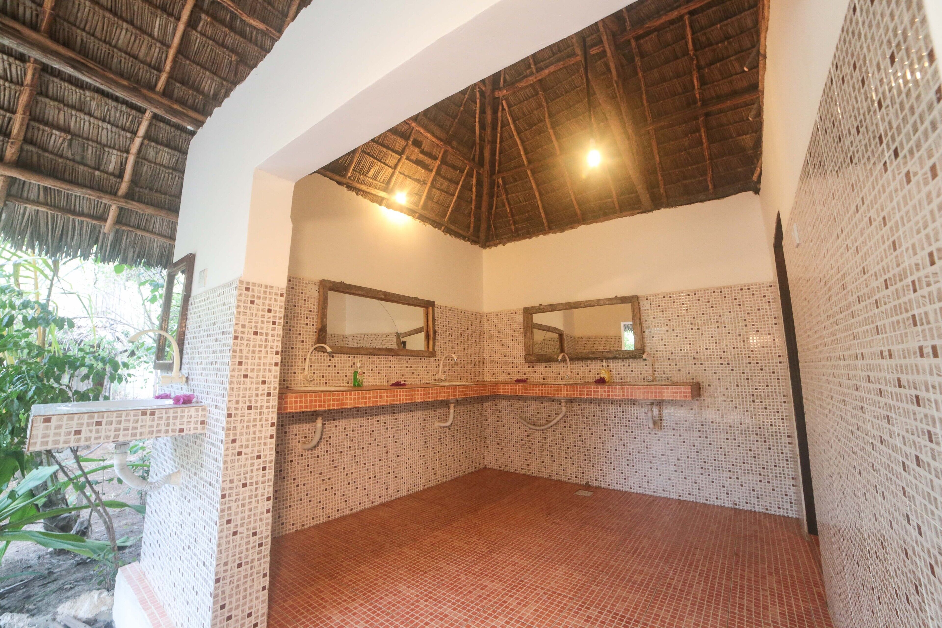 Un baño con dos lavamanos, paredes de azulejos, techo de paja y una ventana pequeña.