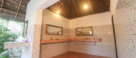 Un baño con dos lavamanos, paredes de azulejos, techo de paja y una ventana pequeña.