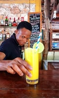 A person at a bar with a drink in front of them. There are bottles and a chalkboard menu in the background.