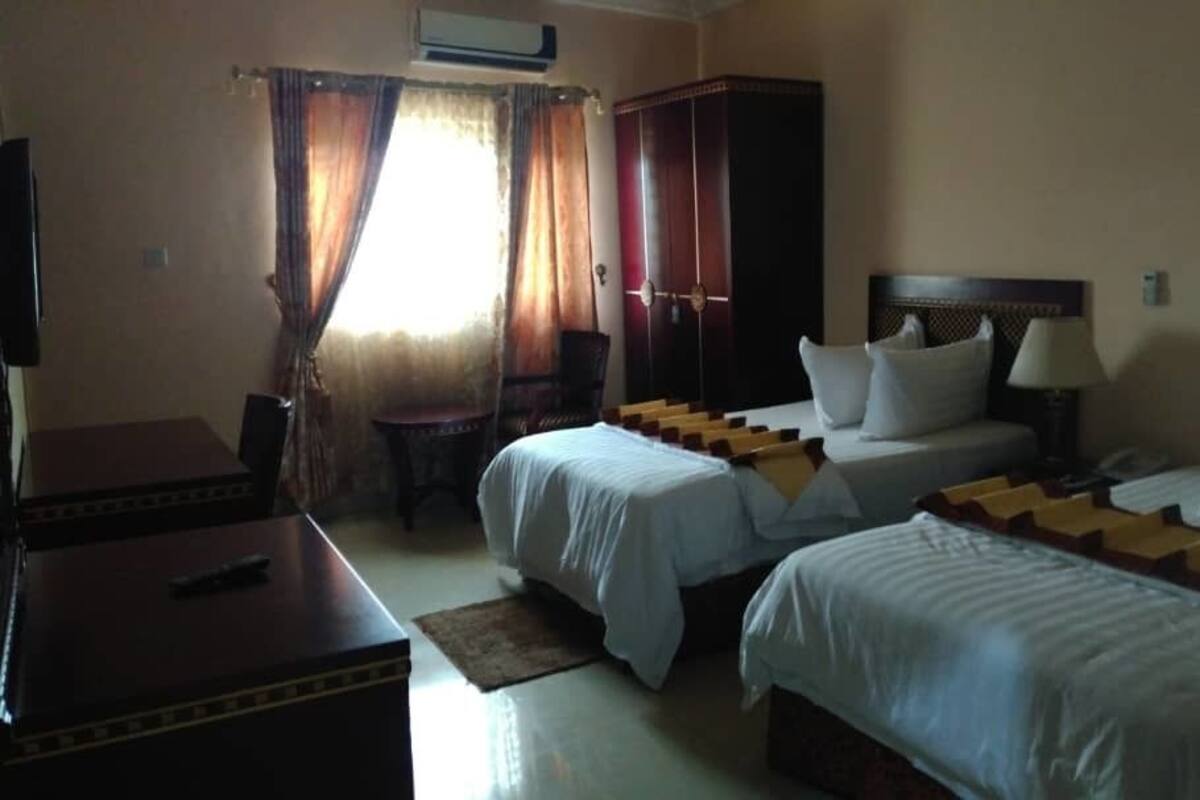 A hotel room with two beds, a desk, a wardrobe, and a TV.