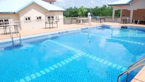 A swimming pool with a tiled pattern, a pool ladder, and a person cleaning the pool. - Obaa'S Golden Plaza Hotel (New Abirem)
