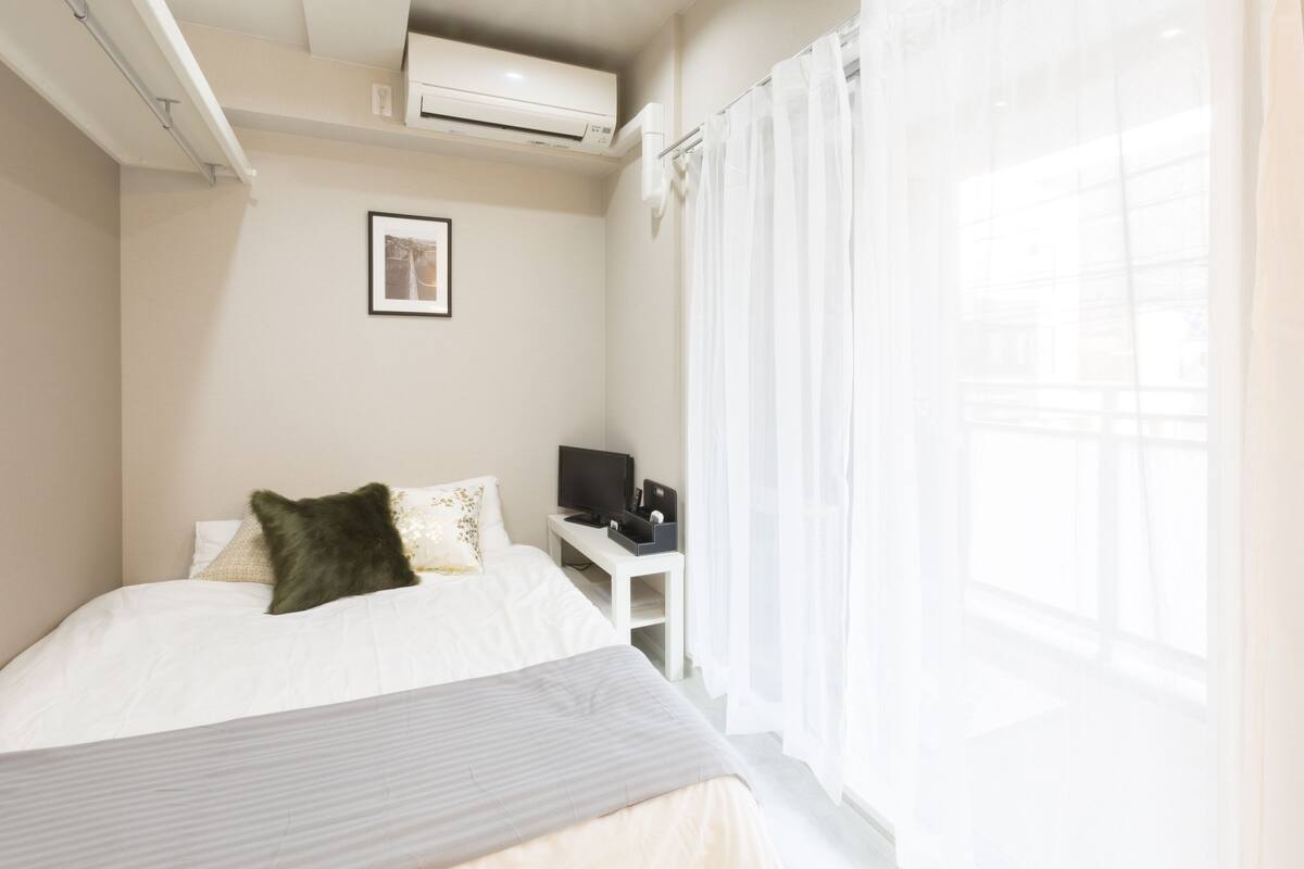 Habitación de hotel con cama, televisor en una mesita auxiliar y ventana con cortinas.