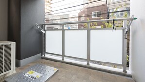 A balcony with a metal railing, a vent, and a window with a view of buildings and power lines. - Jesus Square Nipponbashi (Osaka)