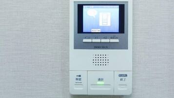 A digital intercom system with a screen displaying a door icon and Japanese text, a keypad, and a speaker.