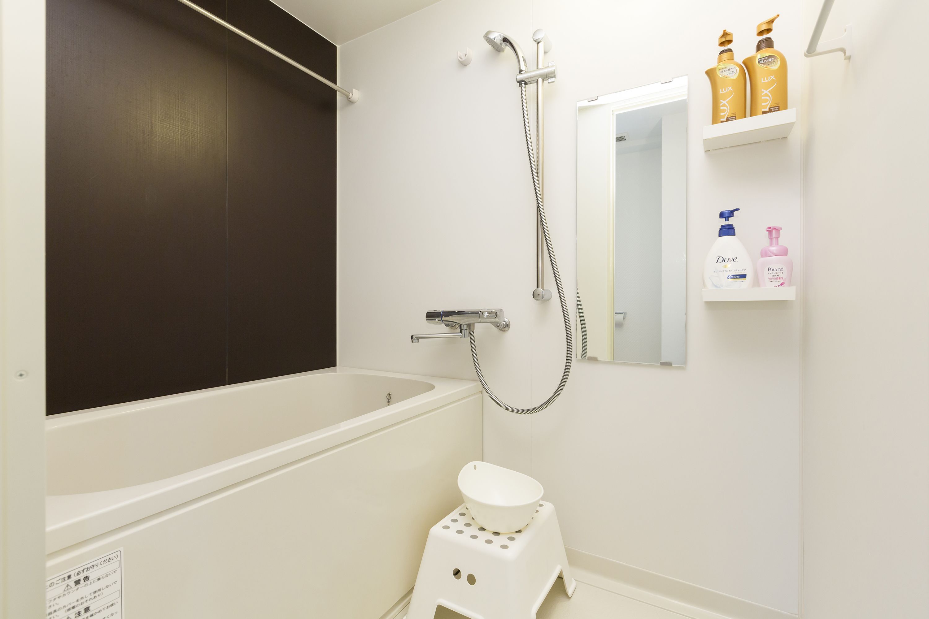 A bathroom with a bathtub, a shower, a toilet, and a shelf with toiletries.