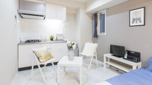 A compact room with a kitchenette, a dining area with a table and chairs, a bed, a television, and a framed picture on the wall. - Jesus Square Nipponbashi (Osaka)