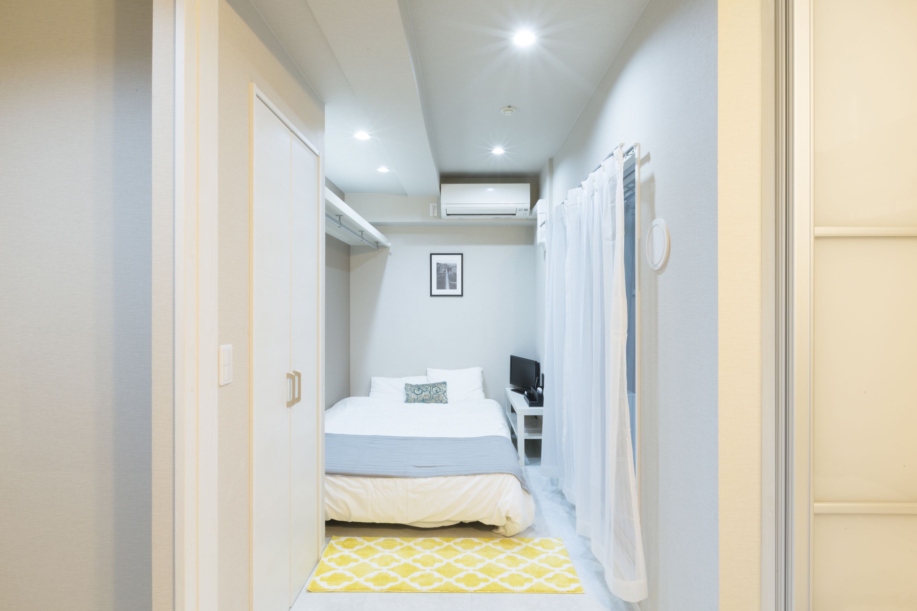 Une chambre d’hôtel étroite, avec un lit, une table de chevet, un petit bureau et une chaise.
