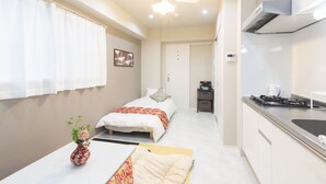 A compact hotel room with a bed, a small kitchenette, a ceiling fan, and a window with curtains. - Jesus Square Nipponbashi (Osaka)