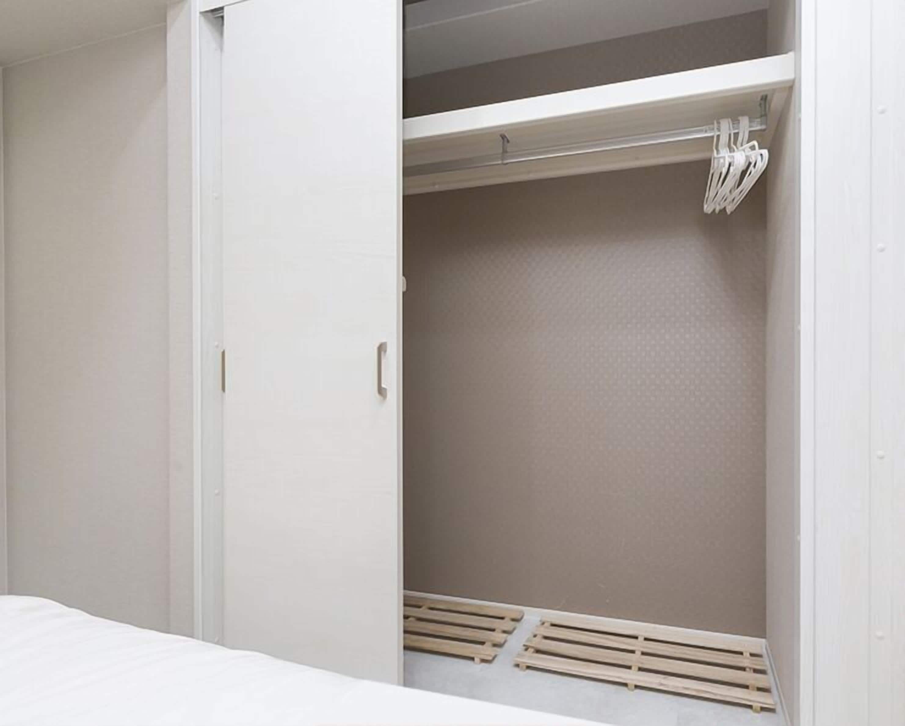 A bedroom with a bed, a wardrobe, and a closet with a hanging rod.