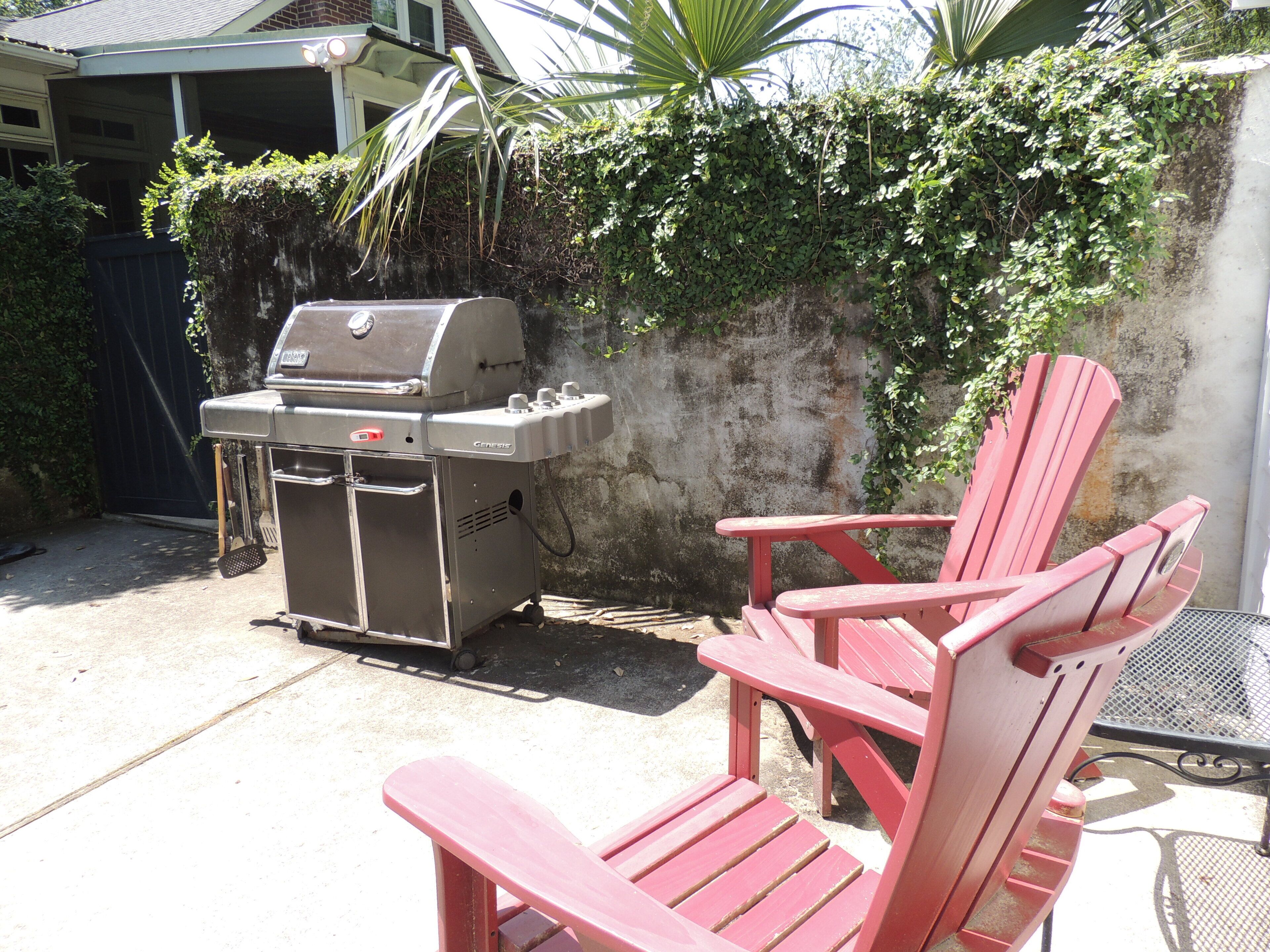 A backyard with a barbecue grill, a red Adirondack chair, and a concrete wall with greenery.