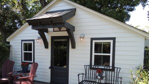 Un petit bâtiment d’un seul étage, doté d’une porte d’entrée sombre, de deux fenêtres et d’un porche avec un banc et deux fauteuils Adirondack.