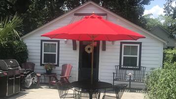 Une maison dotée d’un patio comprenant un parasol rouge, un barbecue et du mobilier d’extérieur.