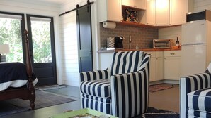 Un espace de vie compact comprenant un coin cuisine, des fauteuils à rayures, une petite table avec un plateau et une valise.