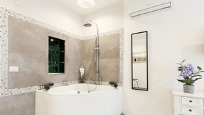 Un baño moderno con una bañera independiente, cabina de ducha de cristal y tocador blanco con una orquídea en maceta.