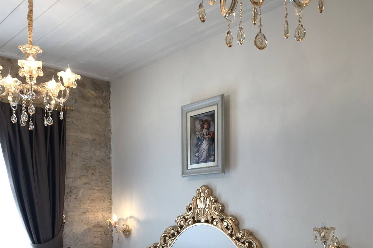 Une chambre d’hôtel avec un grand lit, une tête de lit décorée, un lustre, un tableau encadré au mur et une table de chevet avec une lampe.