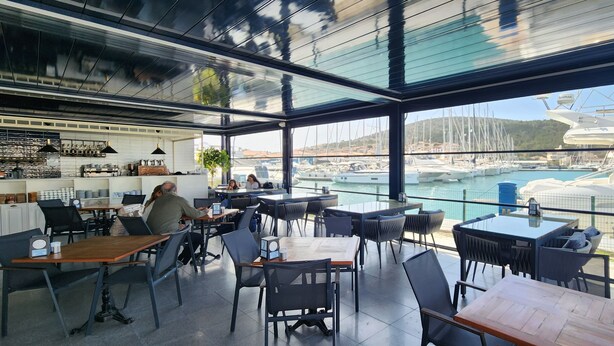 Un restaurant modern amb grans finestres que ofereixen vistes a una marina.