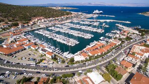 Vista aèria d'una marina plena de vaixells amarrats, envoltada d'edificis residencials i un cel blau clar.