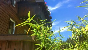 Un bâtiment en bois doté d’un balcon orné de fleurs, un ciel d’un bleu limpide et des bambous au premier plan.