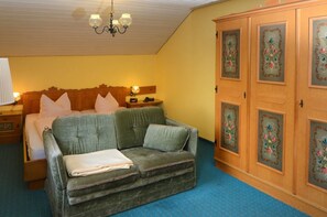 Una habitación con una cama, un sofá verde, un armario de madera con diseños florales y un candelabro.