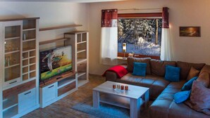 Un salon avec un canapé en cuir marron, un téléviseur posé sur un meuble en bois, une table basse et une fenêtre donnant sur des arbres.