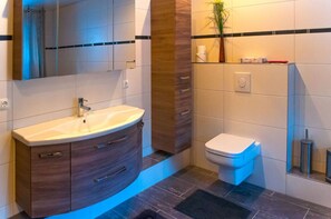 Un baño moderno con tocador, lavabo, espejo, inodoro y una pequeña planta.