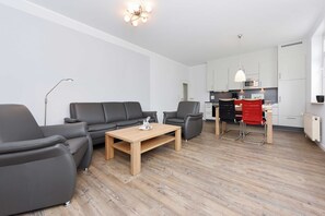 Una sala moderna con sofá, sillas, una mesa de centro y una cocina con armarios y electrodomésticos.