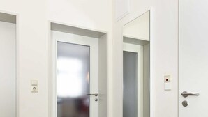 Un corridoio con pavimento in legno, pareti bianche e una porta con finestra in vetro satinato.