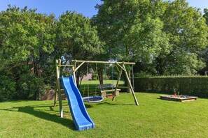 Un parque infantil con un tobogán azul, columpios y un trampolín.