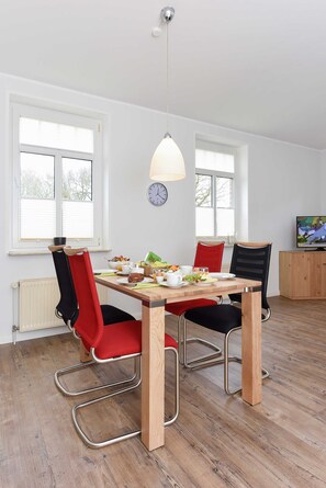 Un comedor con una mesa de madera, sillas rojas y negras, una lámpara colgante y un reloj en la pared.
