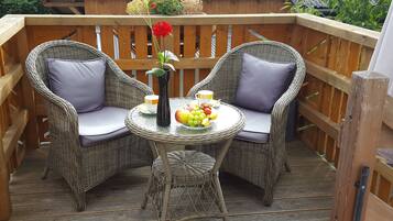 A wicker outdoor seating area with two chairs and a small table, a vase with a flower, and a fruit bowl.